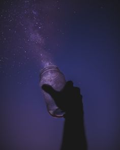 a hand reaching up into the air to reach stars in the night sky with a jar on it