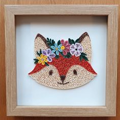 an embroidered fox with flowers on it's head is in a wooden framed frame