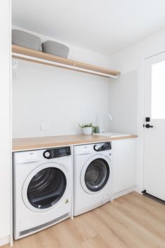 a washer and dryer in a white laundry room with wood flooring on the side