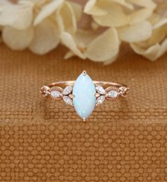 a white opal and diamond ring on top of a brown cloth with flowers in the background