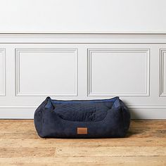 a dog bed sitting on top of a wooden floor next to a white paneled wall