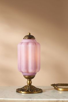 a pink lamp sitting on top of a table next to a gold plated object