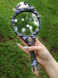 a hand holding a mirror with flowers and leaves on it, in front of a grassy area