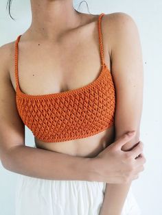 a woman wearing an orange crochet top with her arms crossed in front of her chest