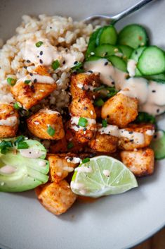 a white plate topped with chicken and rice next to cucumber, lime wedges and cilantro