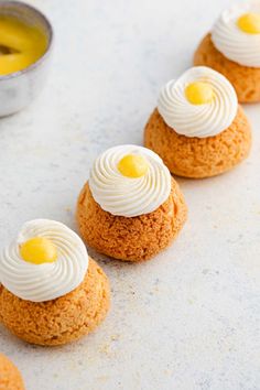 small desserts with white frosting and yellow toppings on a gray surface next to a silver bowl