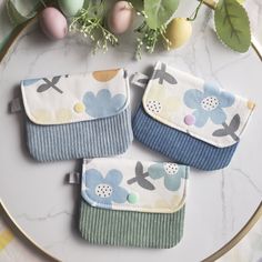 three small wallets sitting on top of a table next to an easter egg and flowers