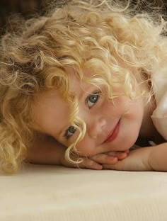 a girl with blonde hair and blue eyes is looking at the camera while she has her hand on her chin