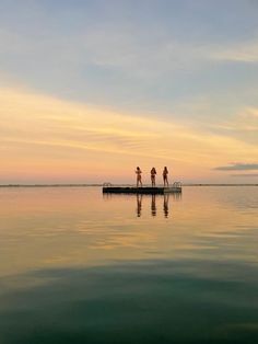 three people are standing on a dock in the middle of the water at sunset or dawn