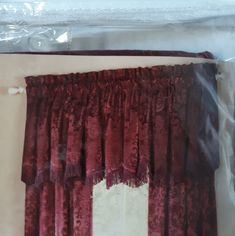 the curtains are red in color and have tassels hanging from them, along with a white wall