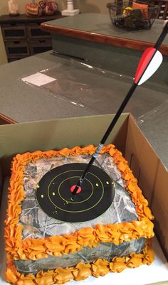 a birthday cake in a box with an arrow sticking out of the center and target on top