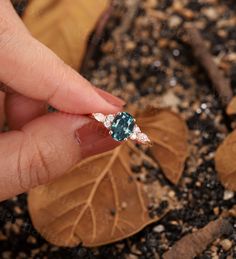 a woman's hand holding an emerald and diamond ring in front of some leaves