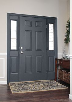 the front door is painted dark gray and has two sidelights on each side, along with a rug