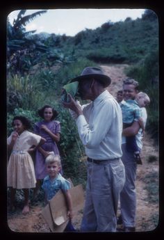 an old photo of a man holding something in his hand while standing next to other people