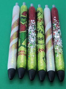 four christmas themed pens are lined up on a green surface with white and red glitters