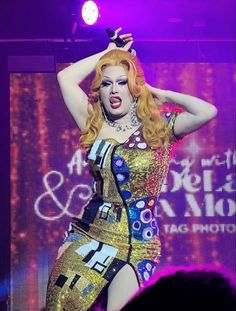 lady in gold and blue outfit on stage with hands behind her head as she sings