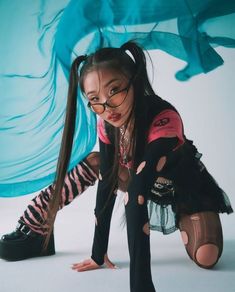 a woman with long hair and glasses kneeling on the ground in front of a blue background