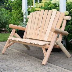 a wooden chair sitting on top of a cement floor next to flowers and bushes in the background