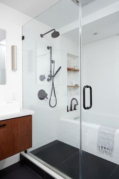 a bathroom with a glass shower door and black floor tiles on the walls, along with a wooden cabinet