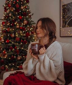 a woman sitting on a couch holding a coffee mug in front of a christmas tree