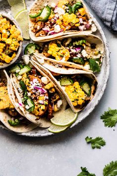 several tacos on a plate with cilantro, lime and other toppings