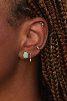 a woman with braids wearing an opal and diamond earring in front of her face