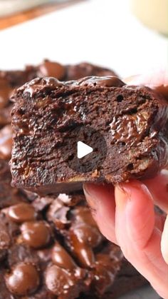 a person holding up a chocolate cookie in front of a pile of brownies on a plate