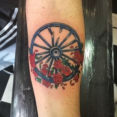 a wheel with roses and leaves on the side of his leg is shown in this tattoo design