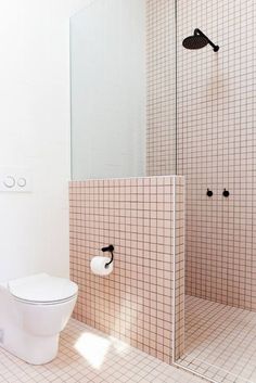 a white toilet sitting inside of a bathroom next to a walk in shower and tiled walls