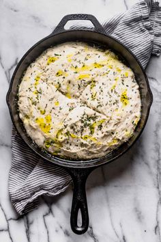 a cast iron skillet filled with mashed potatoes on a marble countertop next to a gray and white dish towel