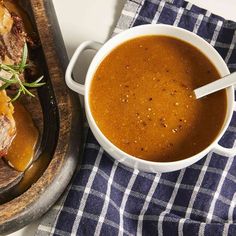 a bowl of soup on a table next to a cutting board with meat and gravy