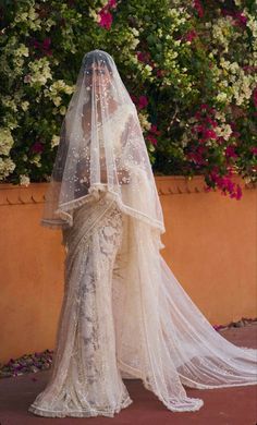 a woman in a wedding dress with a veil on her head and flowers behind her