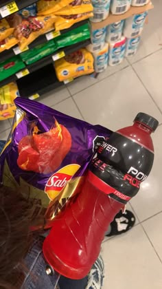 a person holding a bag of chips and a drink in front of a store shelf