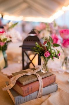 a stack of books sitting on top of a table next to vases filled with flowers