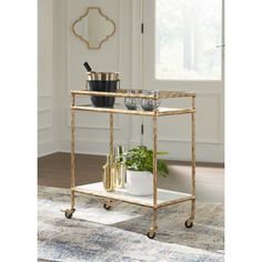 a gold bar cart with drinks on it in front of a window and potted plant