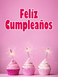 three cupcakes with sparklers in the middle on a pink background that says feliz cumpleanos