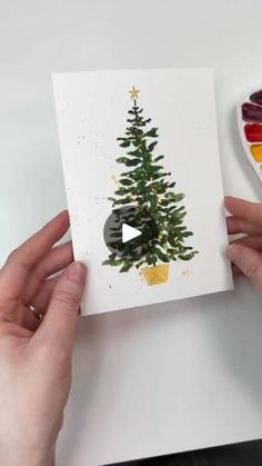 someone holding up a card with a christmas tree on it and paintbrushes next to it