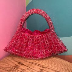 a red purse sitting on top of a wooden table next to a pink and blue wall