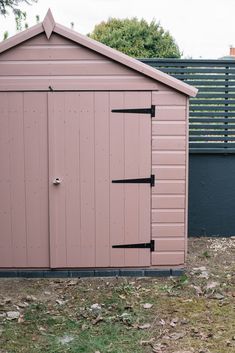 a pink storage shed sitting in the middle of a yard next to a black fence