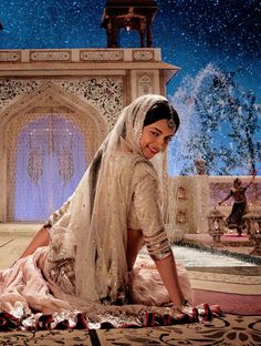 a woman sitting on the ground in front of a fountain wearing a white dress and veil