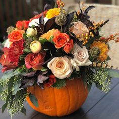 a pumpkin filled with flowers sitting on top of a wooden table