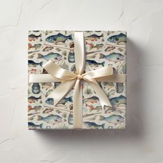 a gift wrapped in white paper with a gold ribbon and fish print on it, tied to a wall