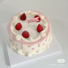 a birthday cake with white frosting and raspberries on top, sitting on a card board