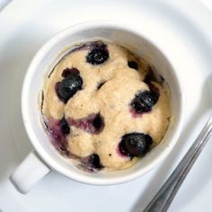 a white plate topped with a bowl of blueberry muffins next to a fork