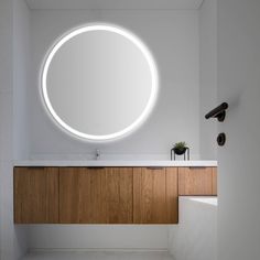 a bathroom with a round mirror on the wall and wooden cabinets below it, along with a plant