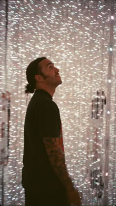 a man standing in front of a white wall covered with beads and chains, looking up at the sky