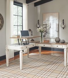 a desk with a laptop on it in front of a window and a painting behind it