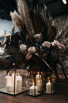 some candles are sitting on a table with dried flowers and feathers in the centerpiece