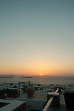 the sun is setting over the ocean and some snow on the ground in front of it