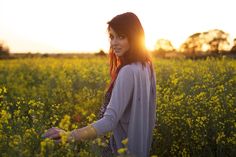 a woman is standing in the middle of a field with yellow flowers and holding her hands out